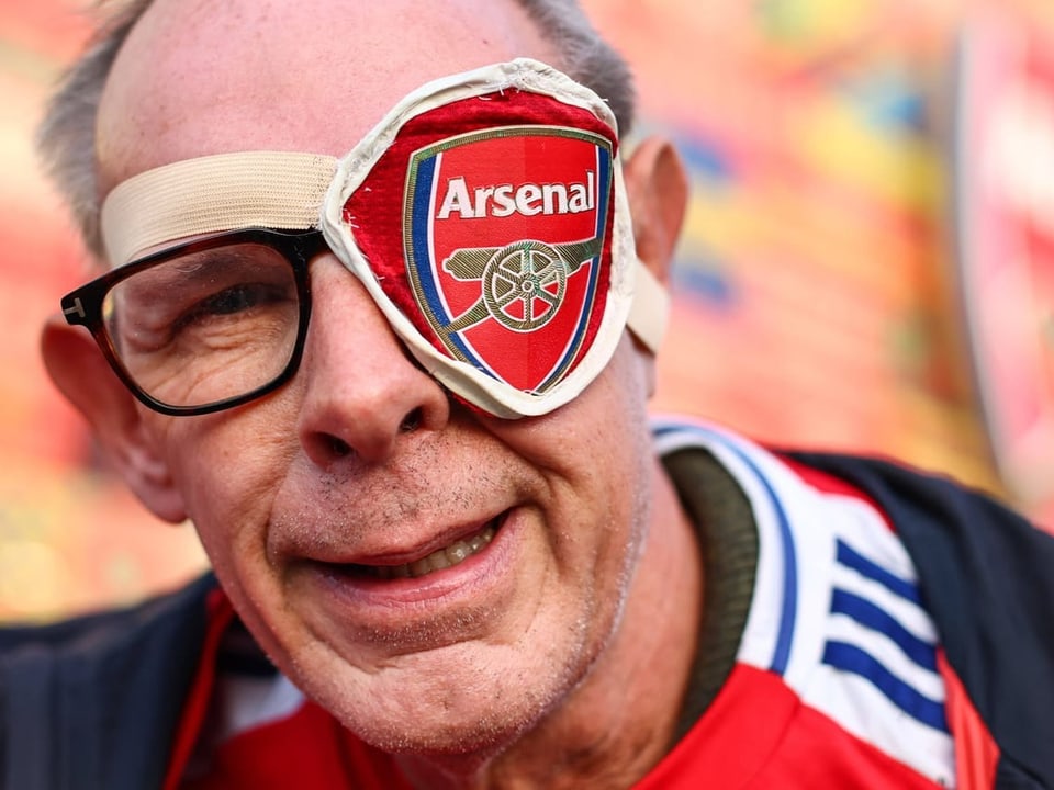 Mann mit Arsenal-Augenklappe und Brille lächelt.