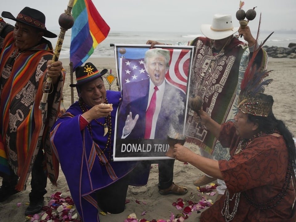 Menschen in traditioneller Kleidung halten Trump-Plakat am Strand.