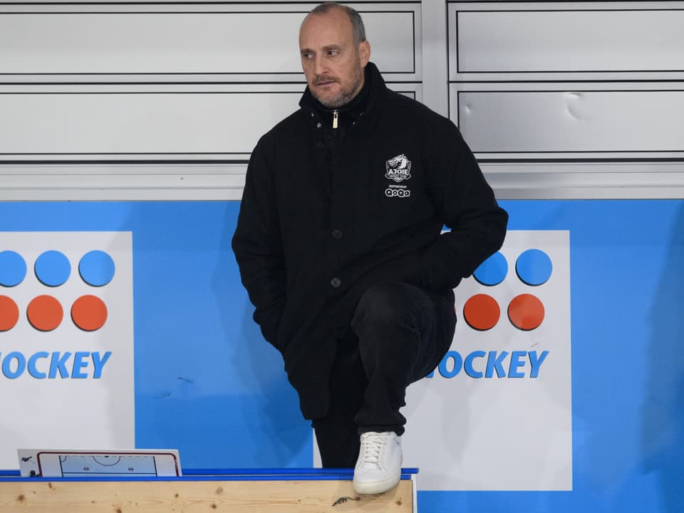 Mann in schwarzer Jacke auf einer Bank in einer Hockeyhalle.