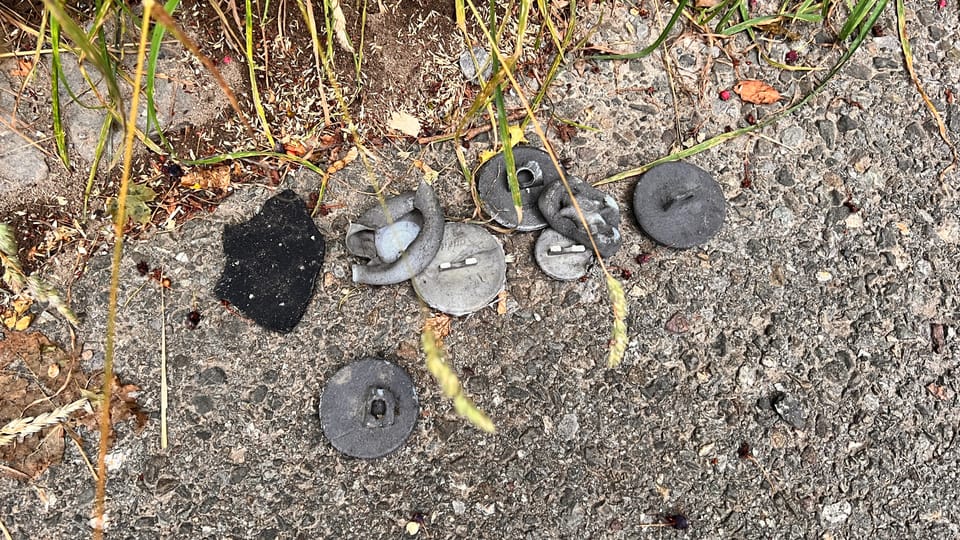 Metallteile und Asphaltstücke auf dem Boden neben Gras.