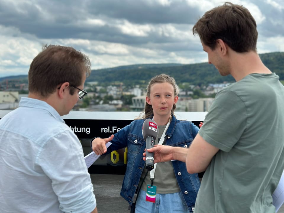 Mädchen interviewt Mann. Ein weiterer Mann steht daneben.