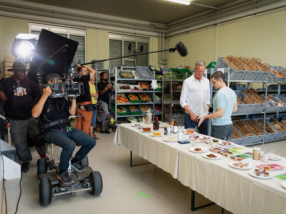 Filmteam filmt zwei Männer vor einem Tisch mit Lebensmitteln in einem Lebensmittelgeschäft.