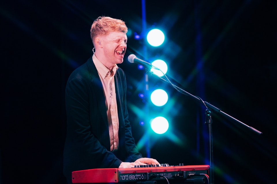 Mann singt und spielt Keyboard auf Bühne.