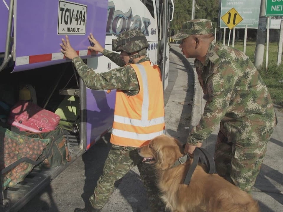 Ein Hund steht mit zwei Soldaten vor einem Car mit Gepäckstücken. 