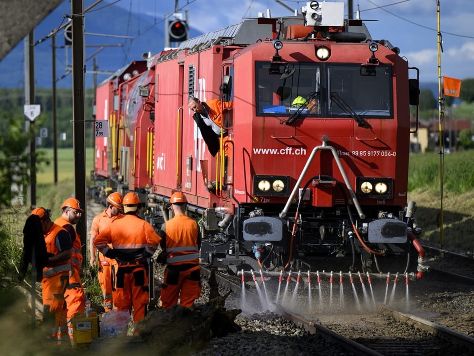 Arbeiter in orangefarbenen Overalls neben rotem Lokomotivzug auf Gleisen