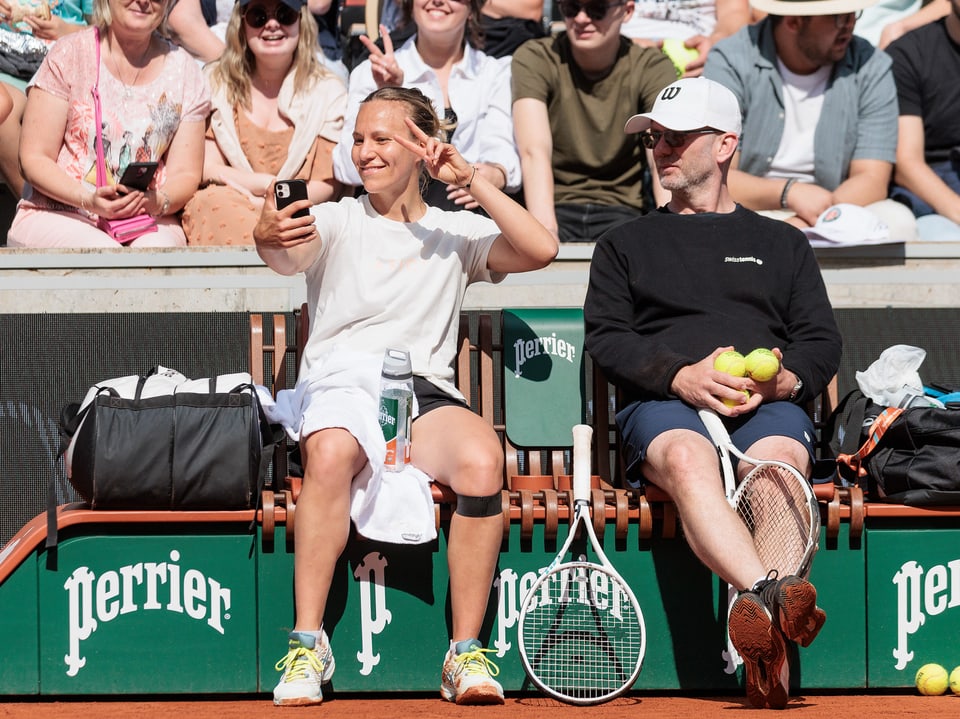 Zwei Personen sitzen auf einer Bank neben einem Tennisplatz.