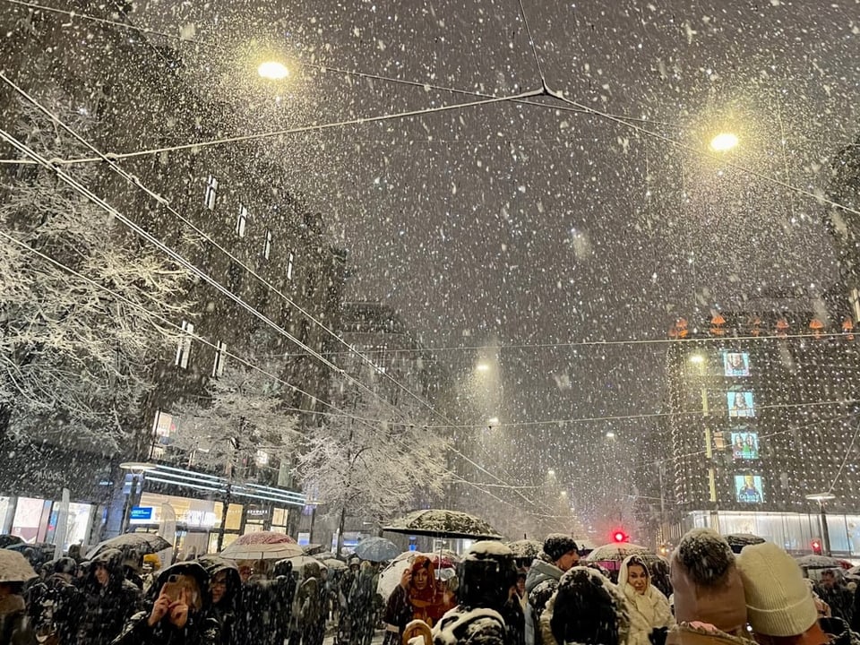 Menschenmenge in verschneiter Stadt bei Nacht.