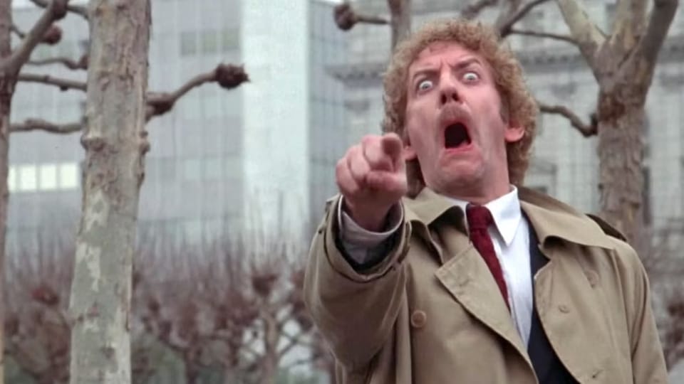 Donald Sutherland mit Anzug und Krawatte. Mit gestrecktem Zeigefinger und weit geöffnetem Mund schaut er in die Kamera.