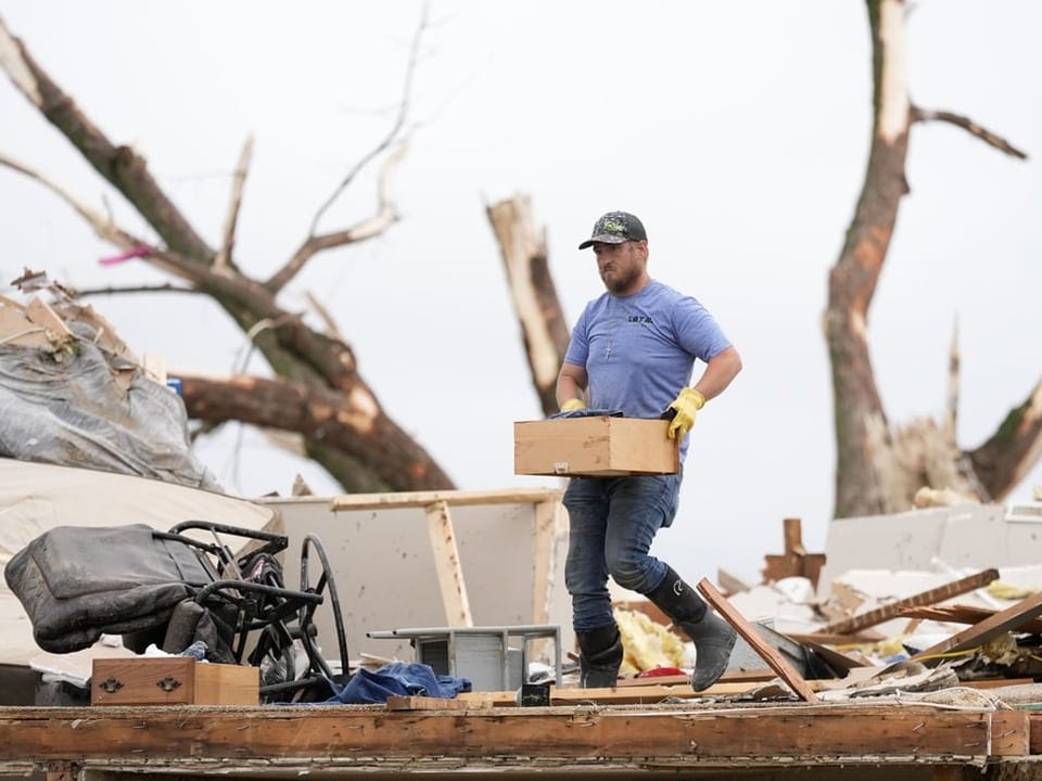 Mann trägt eine Kiste durch Trümmer nach Naturkatastrophe.