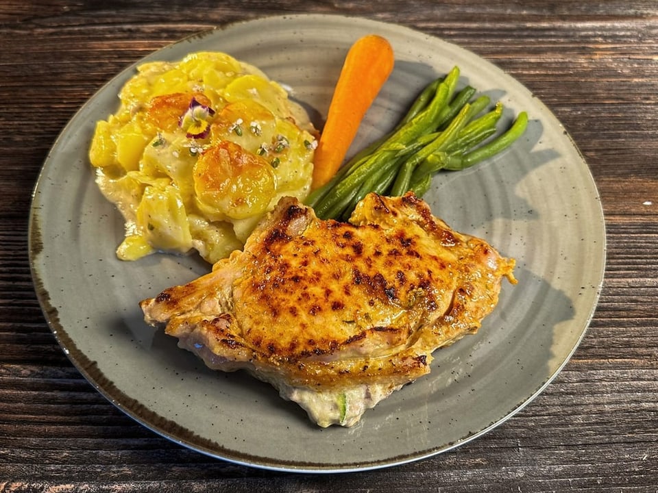 Teller mit Kalbskotelett, Kartoffelgratin, Karotten und Bohnen.