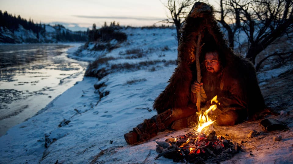 Mann in Pelz am Lagerfeuer im Schnee.