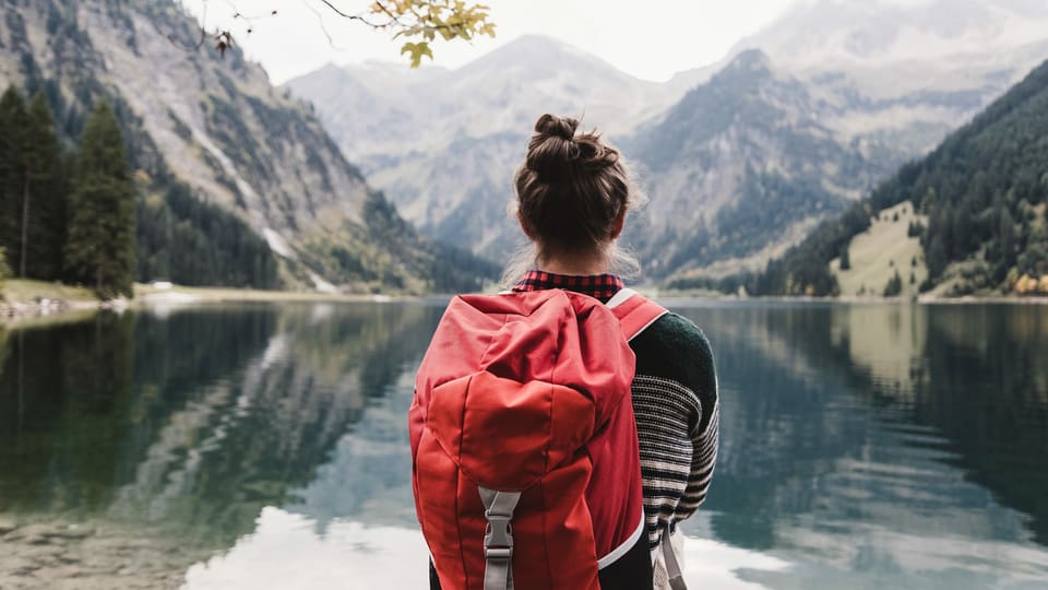 Eine Frau mit Rucksack vor einem Alpsee.