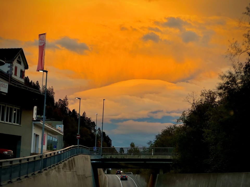 Strasse bei Sonnenuntergang mit Brücke und dramatischem Himmel.