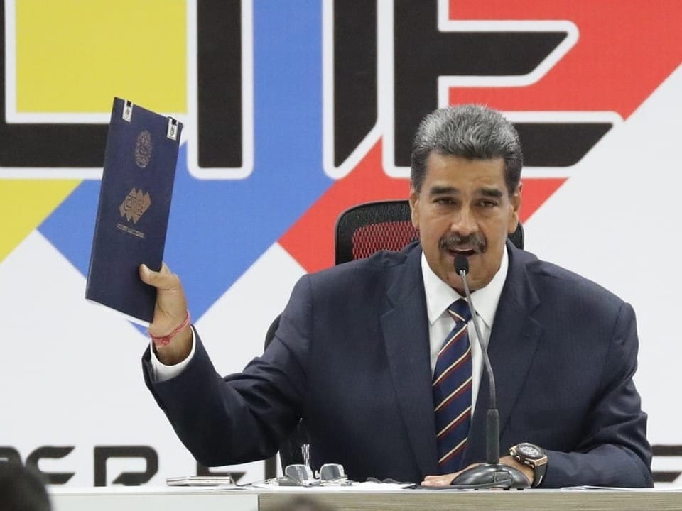 Maduro sitzt hinter einem Mikrofon. 