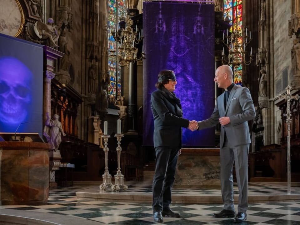 Zwei Männer schütteln sich in einer Kathedrale die Hand bei Kunstinstallation.