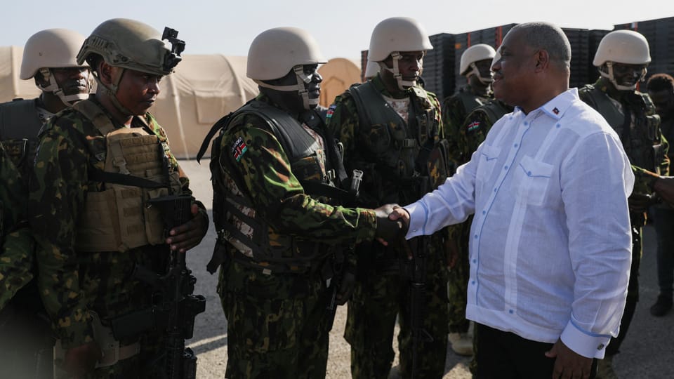 Garry Conille in weissem Hemd schüttelt kenianischen Soldaten in Tarnkleidung die Hand.