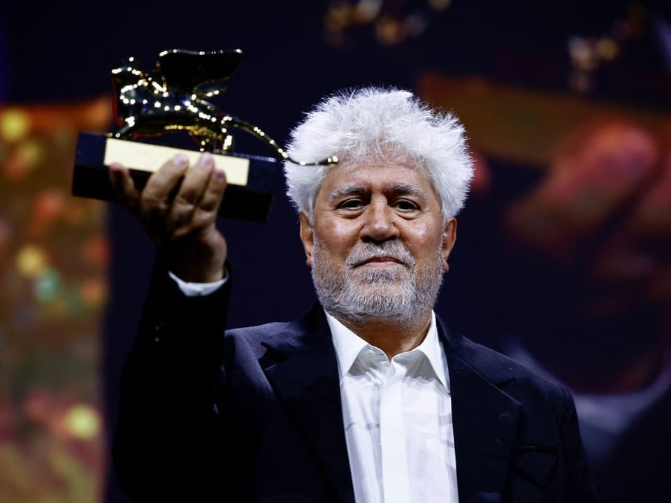 Pedro Almodóvar hält Trophäe hoch.