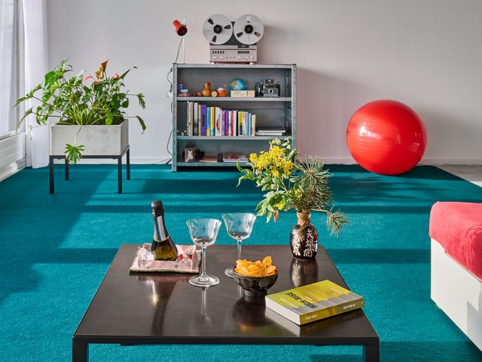 Wohnzimmer mit Tisch, Blumen, Büchern, Pflanzen, Retro-Bandrekorder und rotem Gymnastikball.