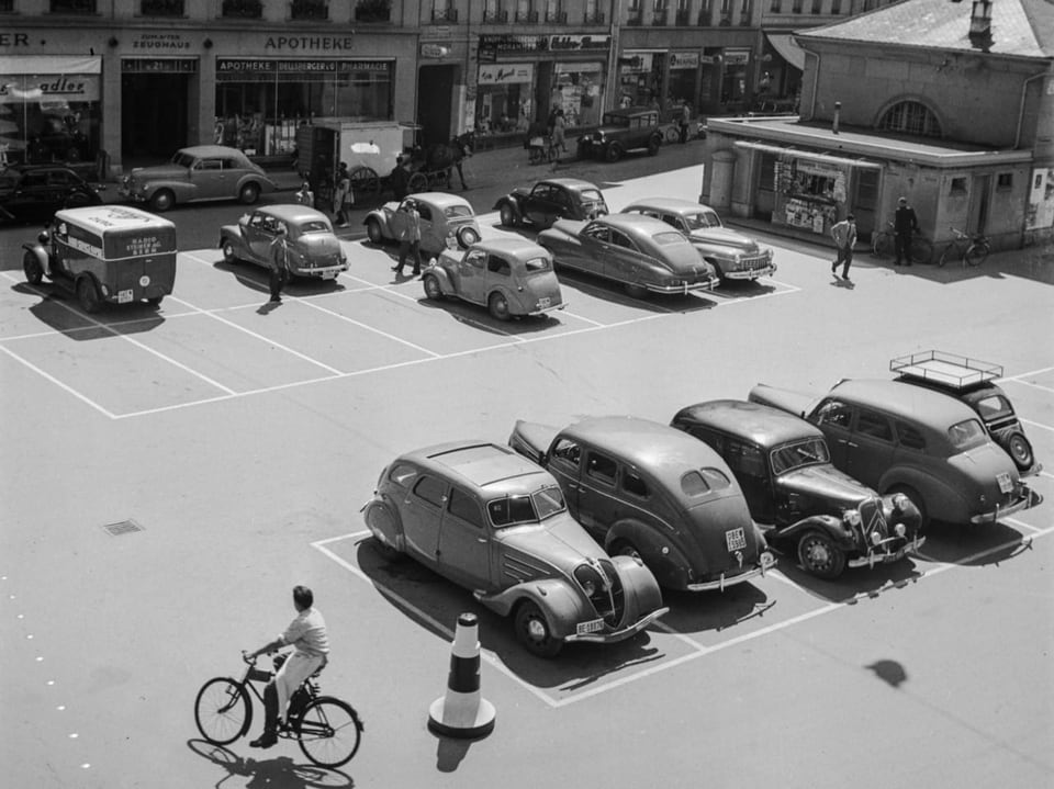 Parkplatz mit Oldtimern und Radfahrer in einer Stadt.