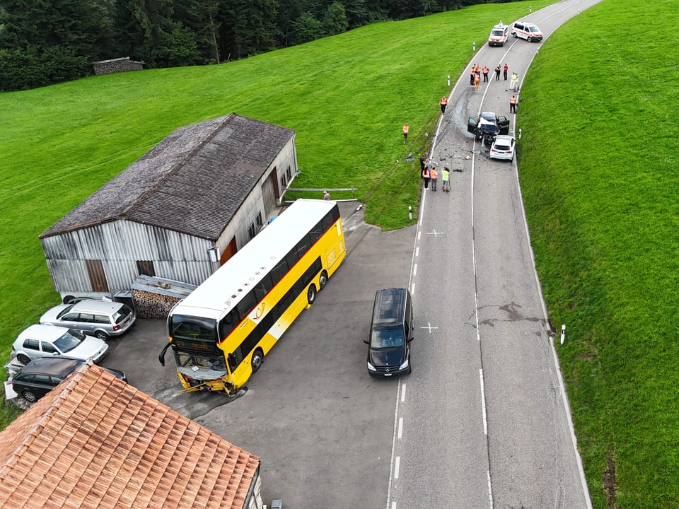 Polizisten bei der Unfallstelle mit zwei beschädigten Pkw und einem Postauto.