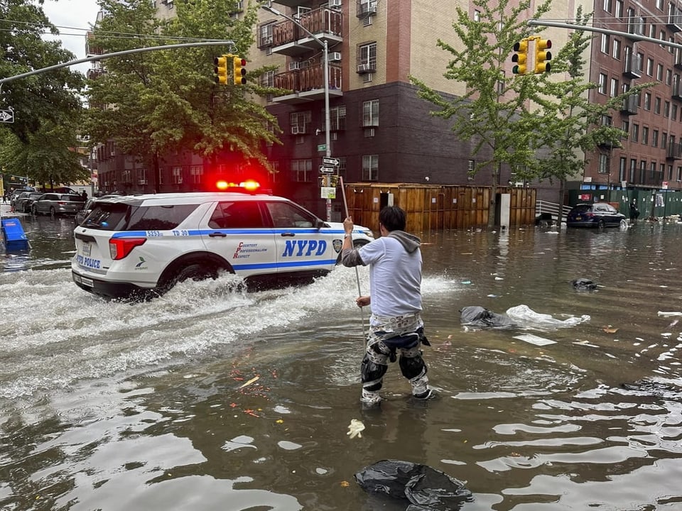 Überflutete Strasse im New Yorker Stadtbezirk Brooklyn: Ein Mann steht knietief im Wasser, ein Polizeiauto fährt vorbei.