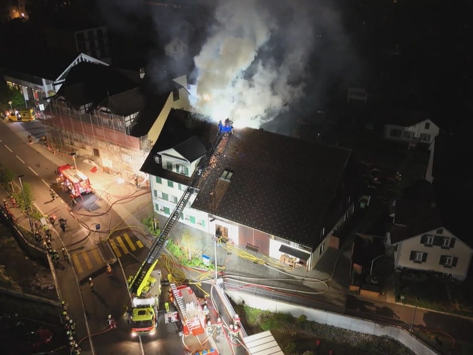 Nachtluftaufnahme von Feuerwehrleuten, die einen Grossbrand in einem Gebäudekomplex bekämpfen.