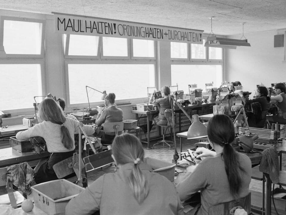 Mädchen in Arbeitsraum. Banner mit Aufschrift: «Maulhalten! Ordnung halten + Durchhalten»