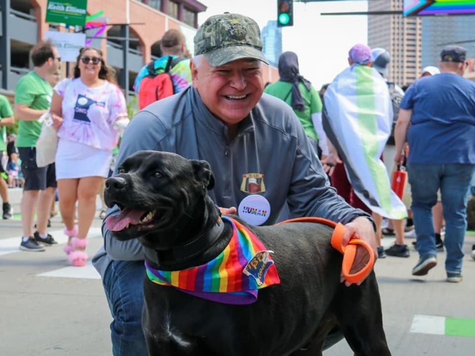 Mann mit Hund, trägt Regenbogen-Halstuch bei einer Parade.