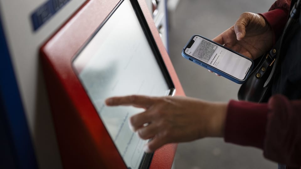 Person verwendet Handy und berührt Bildschirm am Automaten.