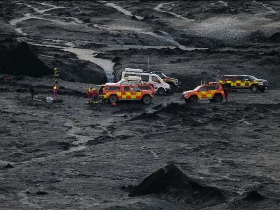 Rettungsfahrzeuge und Arbeitskräfte auf einem Aschefeld.