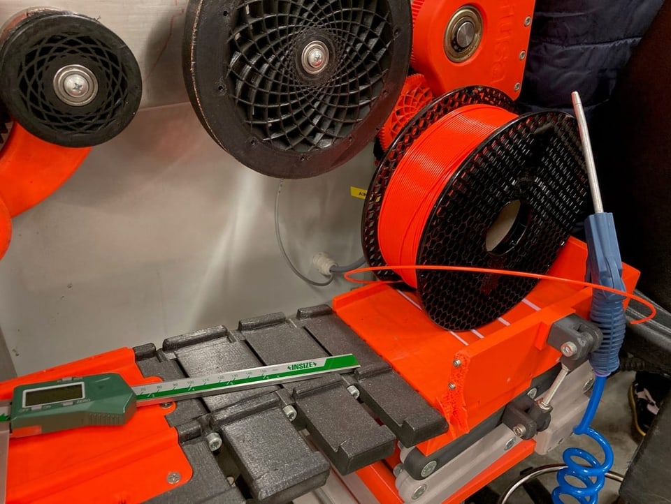 Eine volle Rolle mit orangem Plastikfaden ist in eine Maschine eingespannt.
