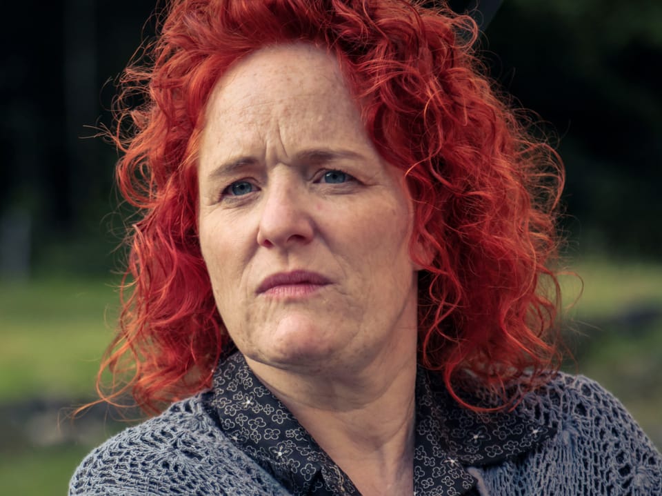 Eine Frau mit leuchtend roten Haaren schaut skeptisch.
