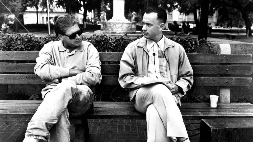 Zwei Männer sitzen auf einer Parkbank und schauen sich an.