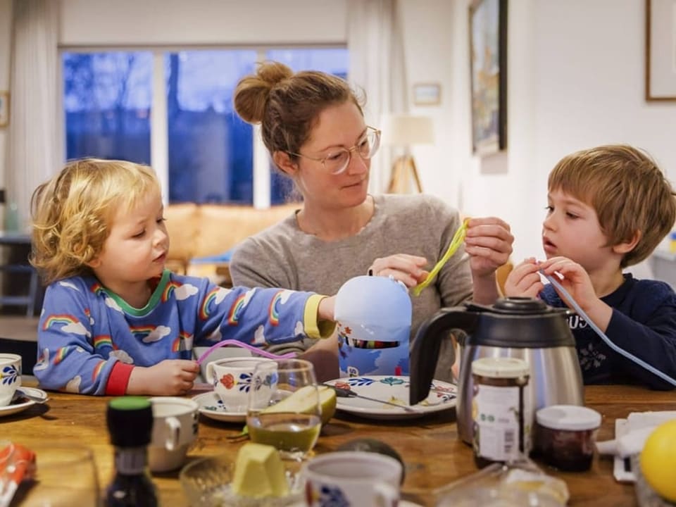 Mutter bastelt mit zwei Kindern am Frühstückstisch.