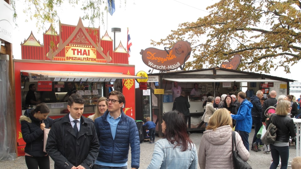 Leute an einem Jahrmarkt vor einem Essstand der Thai-Küche anbietet. 