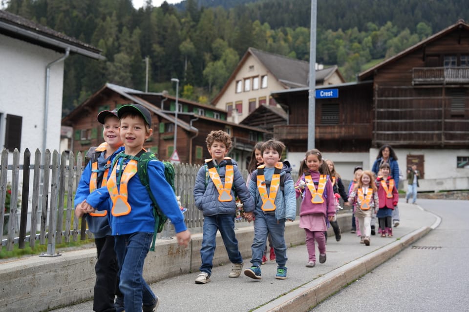 Kindergruppe in Sicherheitswesten spaziert auf ländlicher Strasse.