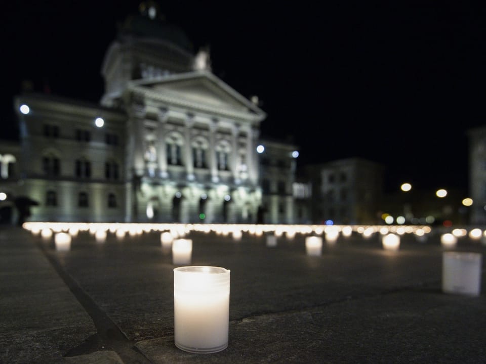 Kerzen vor einem beleuchteten Gebäude bei Nacht.