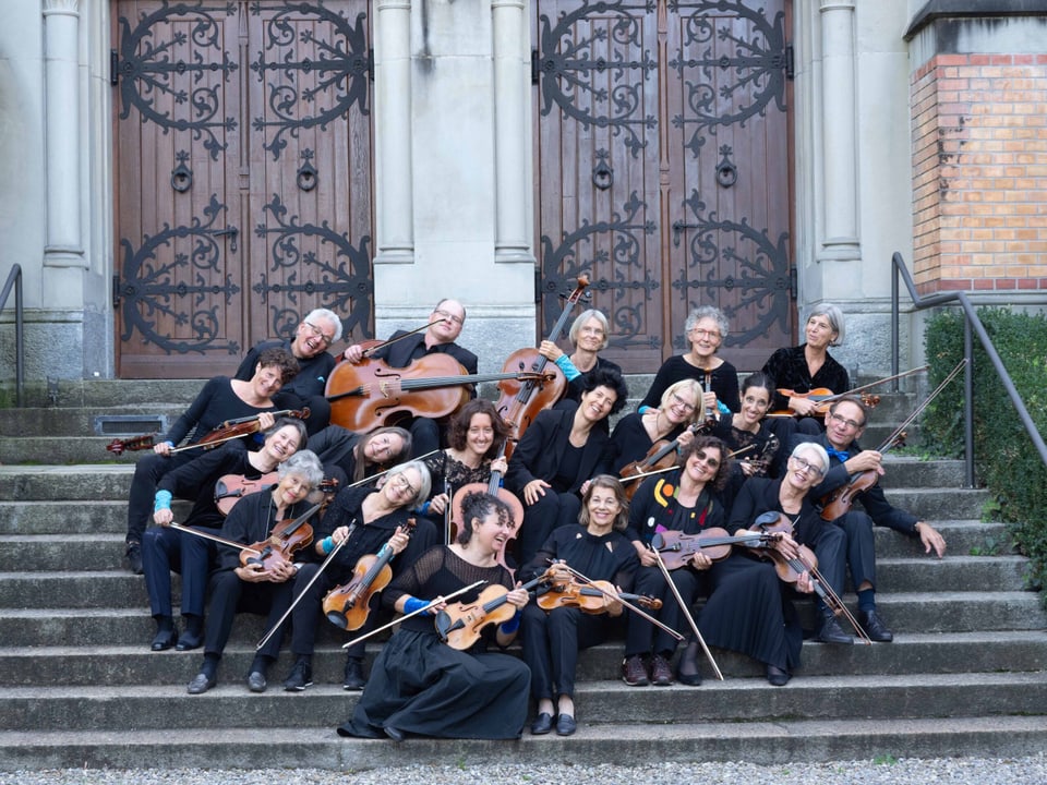 Musikerinnen und Musiker der Orchestrina sitzen auf einer Treppe, alle sind nach rechts geneigt.