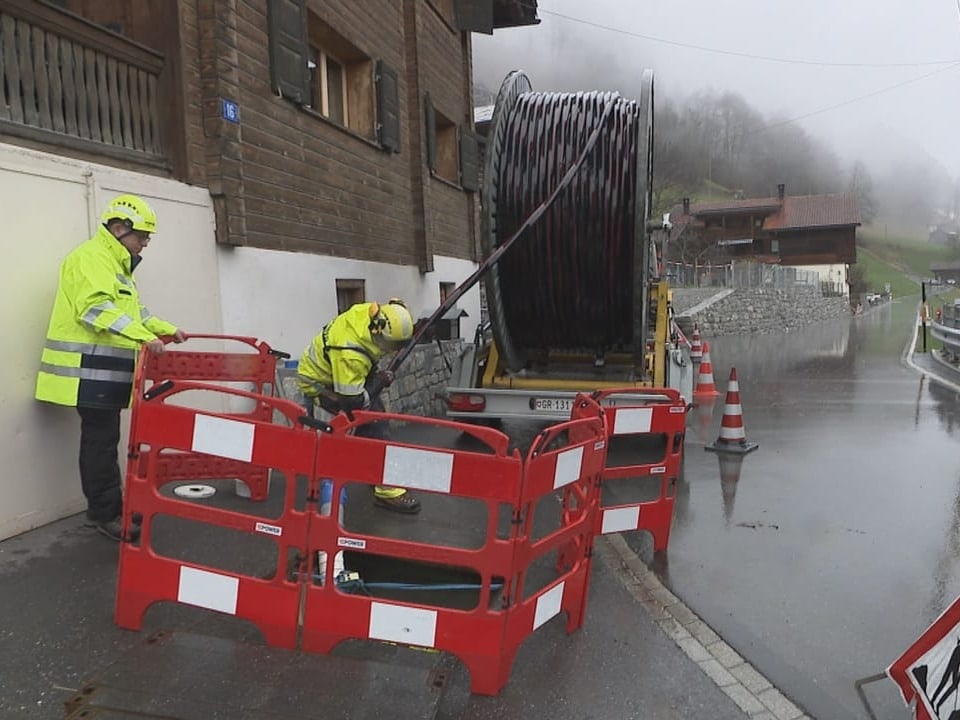 Zwei Männer stehen auf dem Trottoir vor einem Loch mit einem grossen schwarzen Schlauch. 