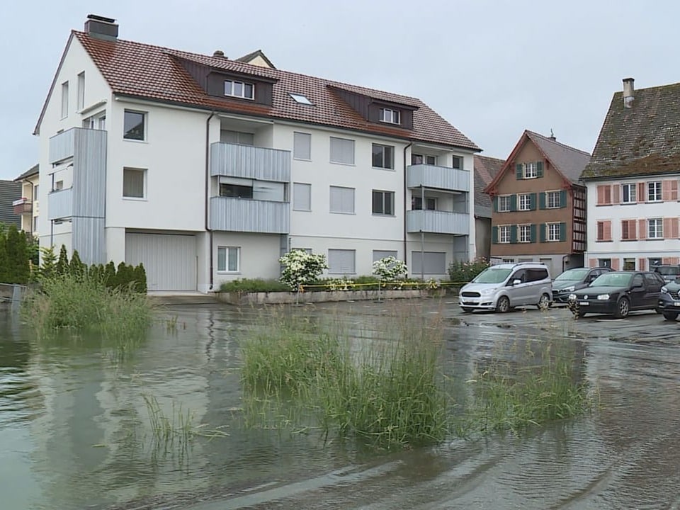 Überfluteter Parkplatz vor mehrstöckigen Wohnhäusern.