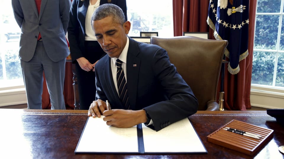 Barack Obama unterzeichnet an einem Schreibtisch ein Dekret.