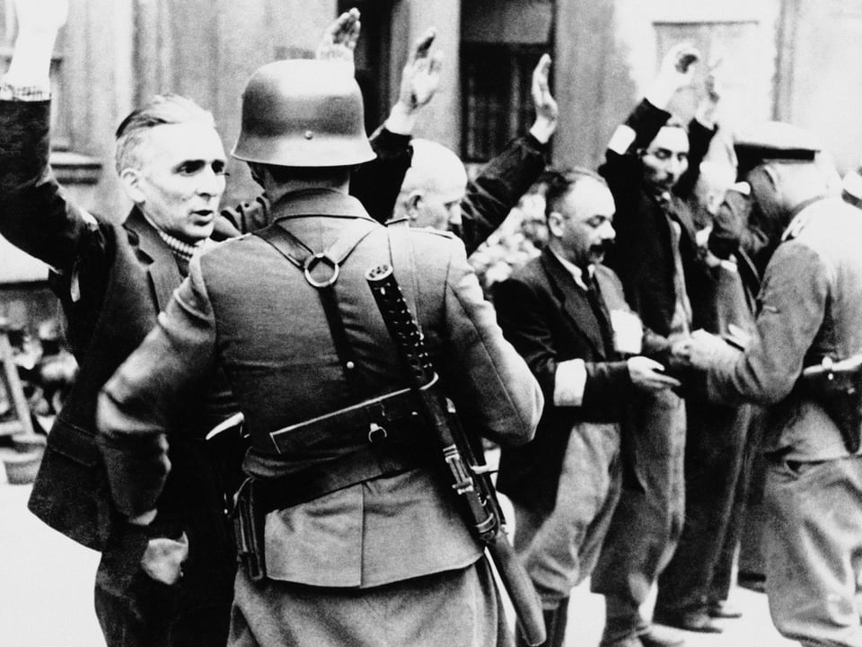 Schwarz-weiss-Bild: Soldaten bedrohen Juden mit erhobenen Händen.