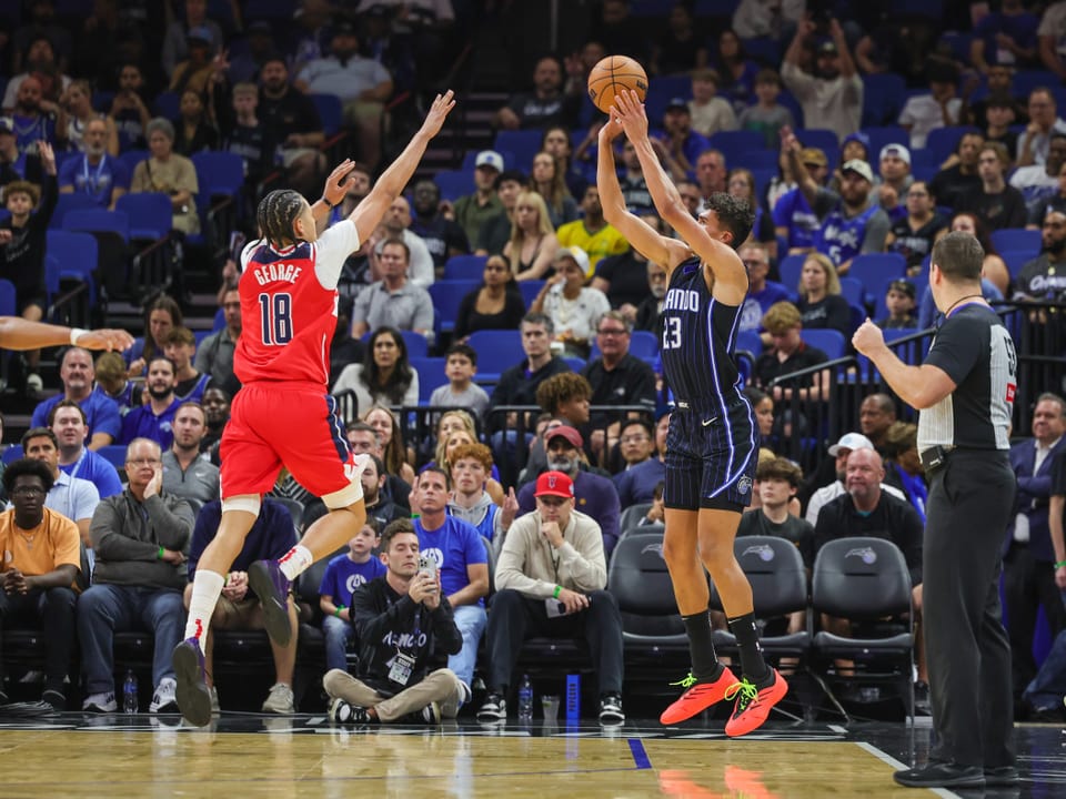 Basketballspieler beim Wurf, Gegenspieler springt zum Block.