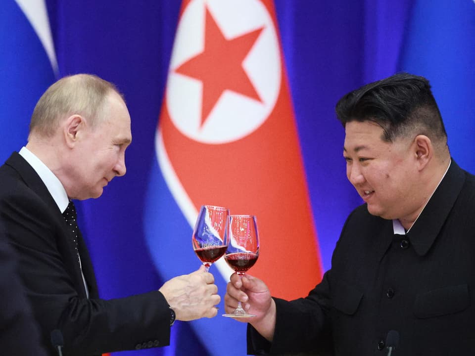 Wladimir Putin und Kim Jong-Un stossen mit Weingläsern an, nordkoreanische Flagge im Hintergrund.