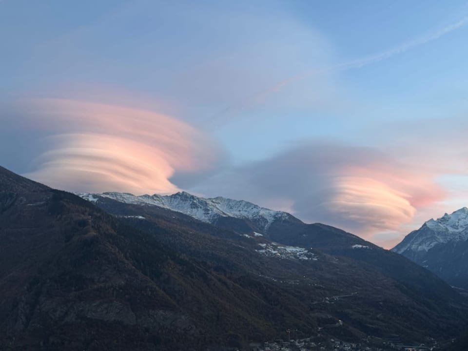 Lenticularis-Wolken über schneebedeckten Bergen im Abendlicht.