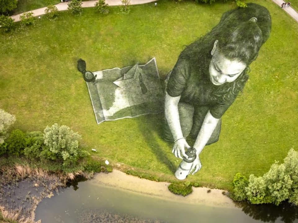 Luftaufnahme einer Wiese mit riesigem Bild einer Frau, Bäumen und einem Fluss.