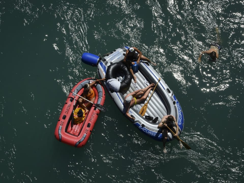 Zwei Schlauchboote mit Menschen auf einem Fluss, eine Person schwimmt daneben.