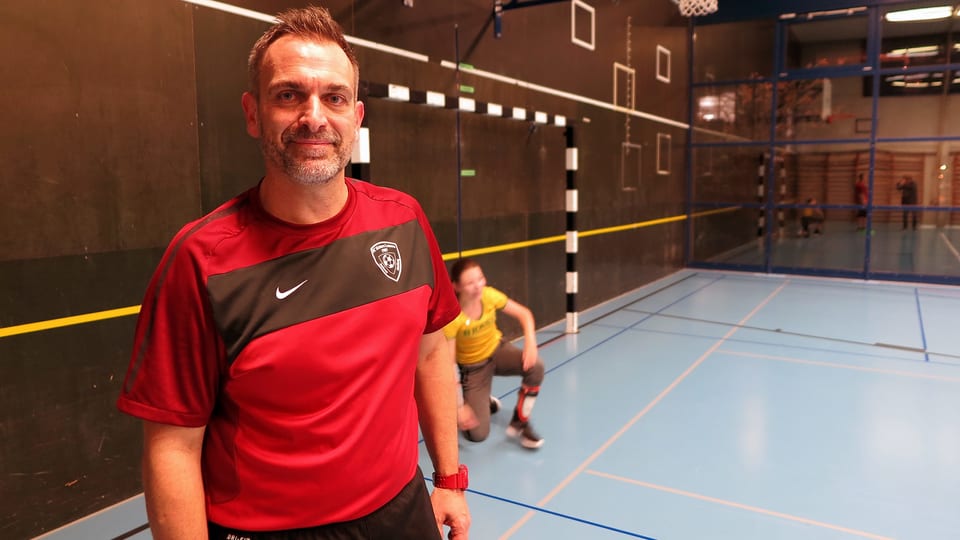 Ein Mann in einer Turnhalle. Er trägt ein rot-schwarzes Fussball-Shirt mit dem Emblem des FC Kickers Luzern.  