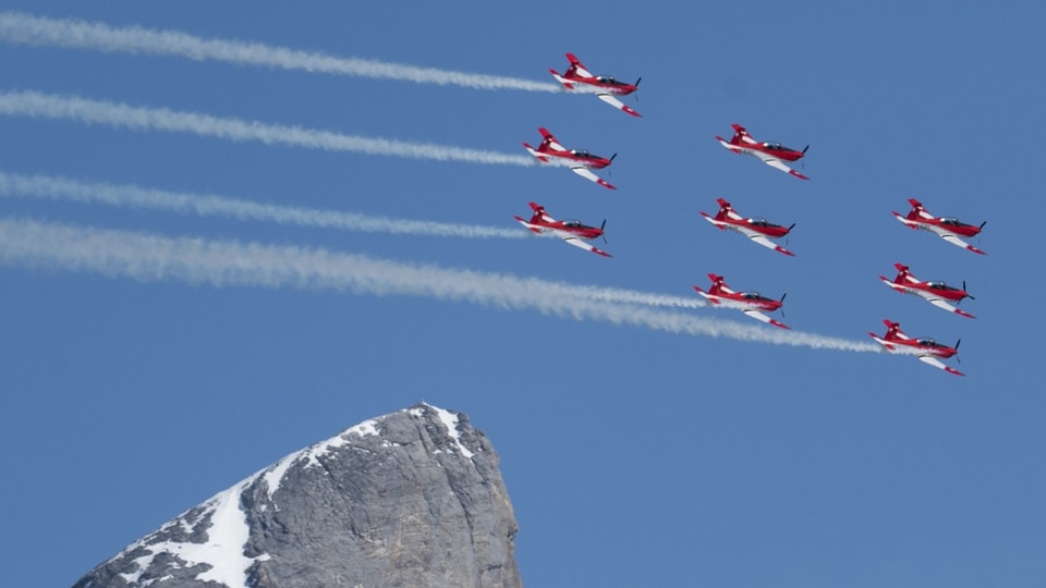 Neun rot-weisse Flugzeuge fliegen über einen Berggifpel.