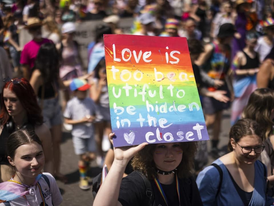Eine Person hält ein Schild in die Luft mit der Aufschrift «Love is too beautiful to be hidden in the closet»